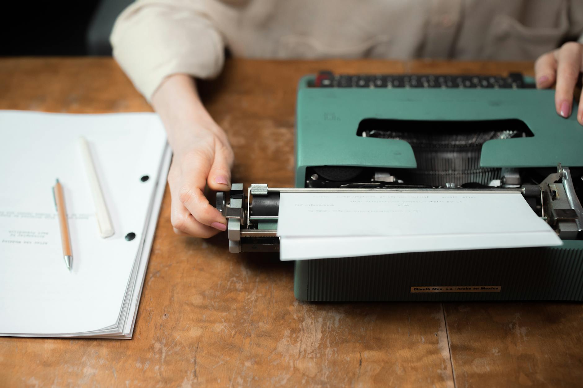 Close-up of hands typing on a vintage green typewriter with papers on a wooden desk.