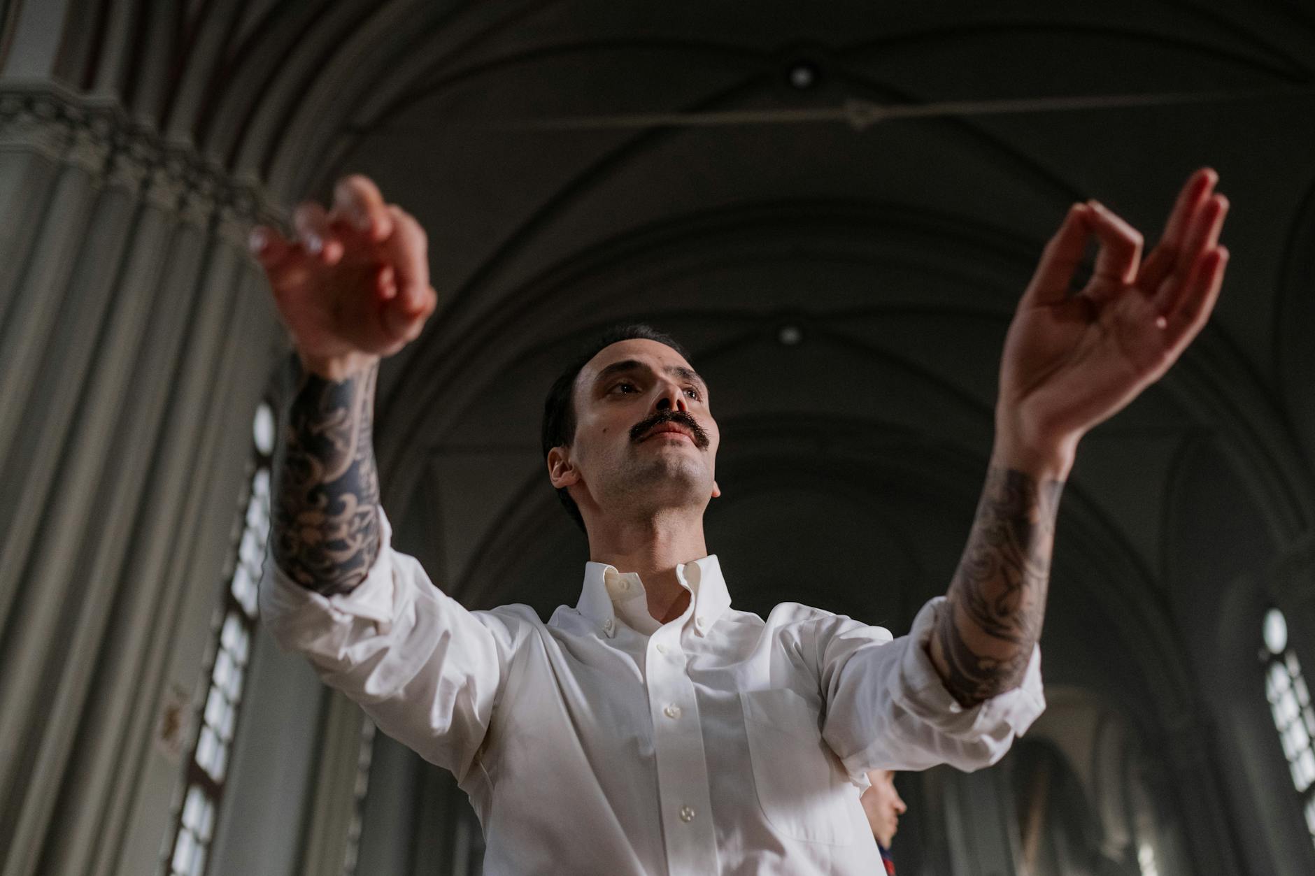 Tattooed conductor with a mustache dynamically directs music in an indoor venue.