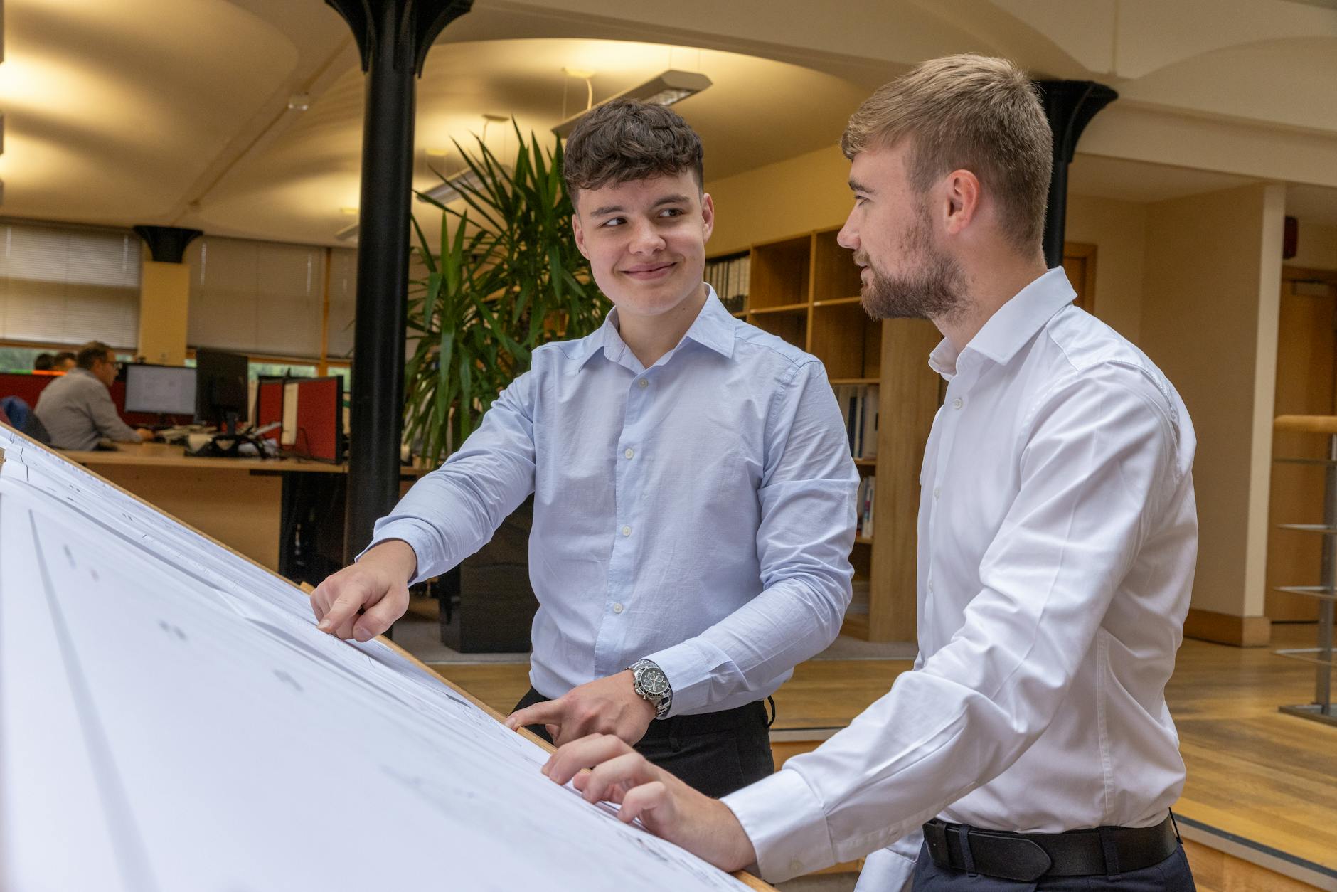 Two young professionals discussing plans in a modern, well-lit office setting.