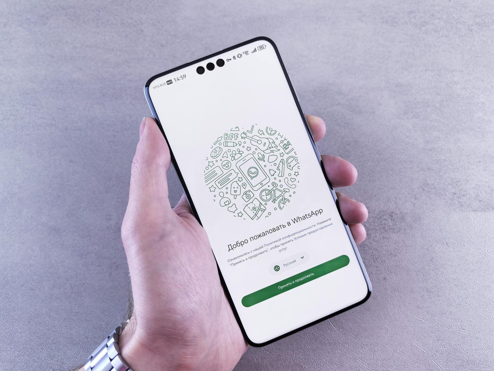 Close-up of a hand holding a smartphone displaying the WhatsApp welcome screen in Russian.