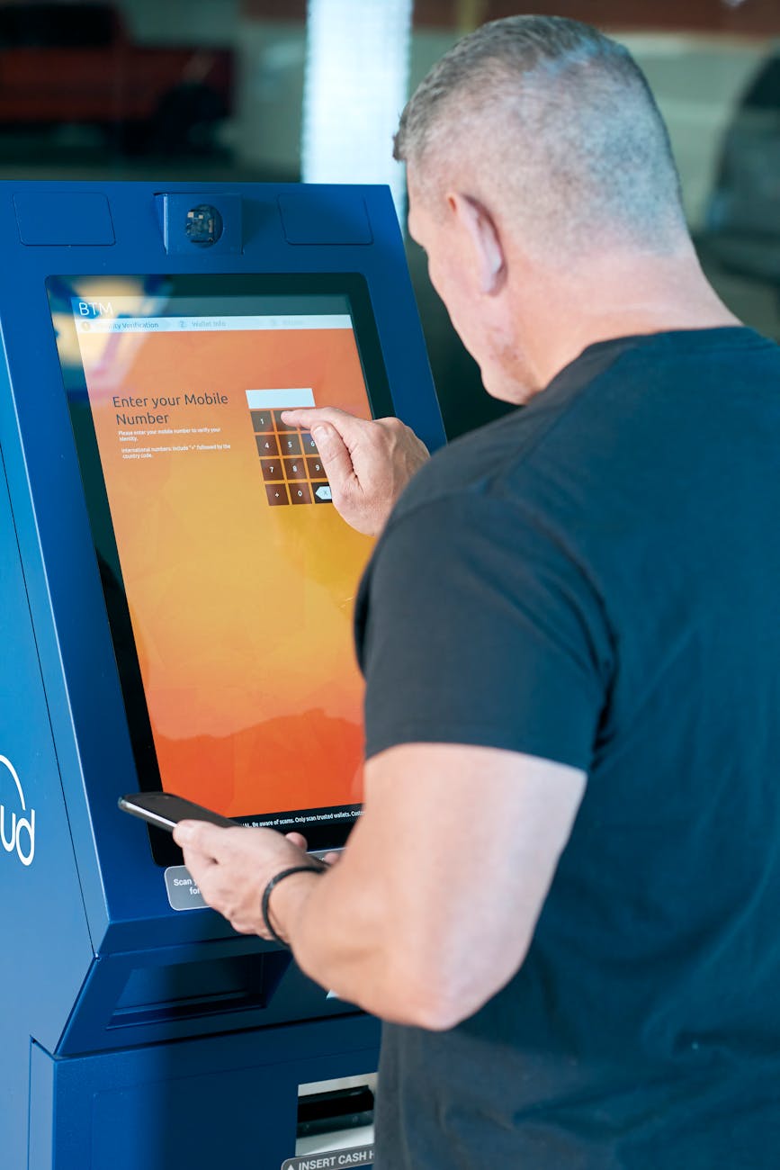 Man interacts with a touchscreen ATM, entering mobile number. Modern technology in action.