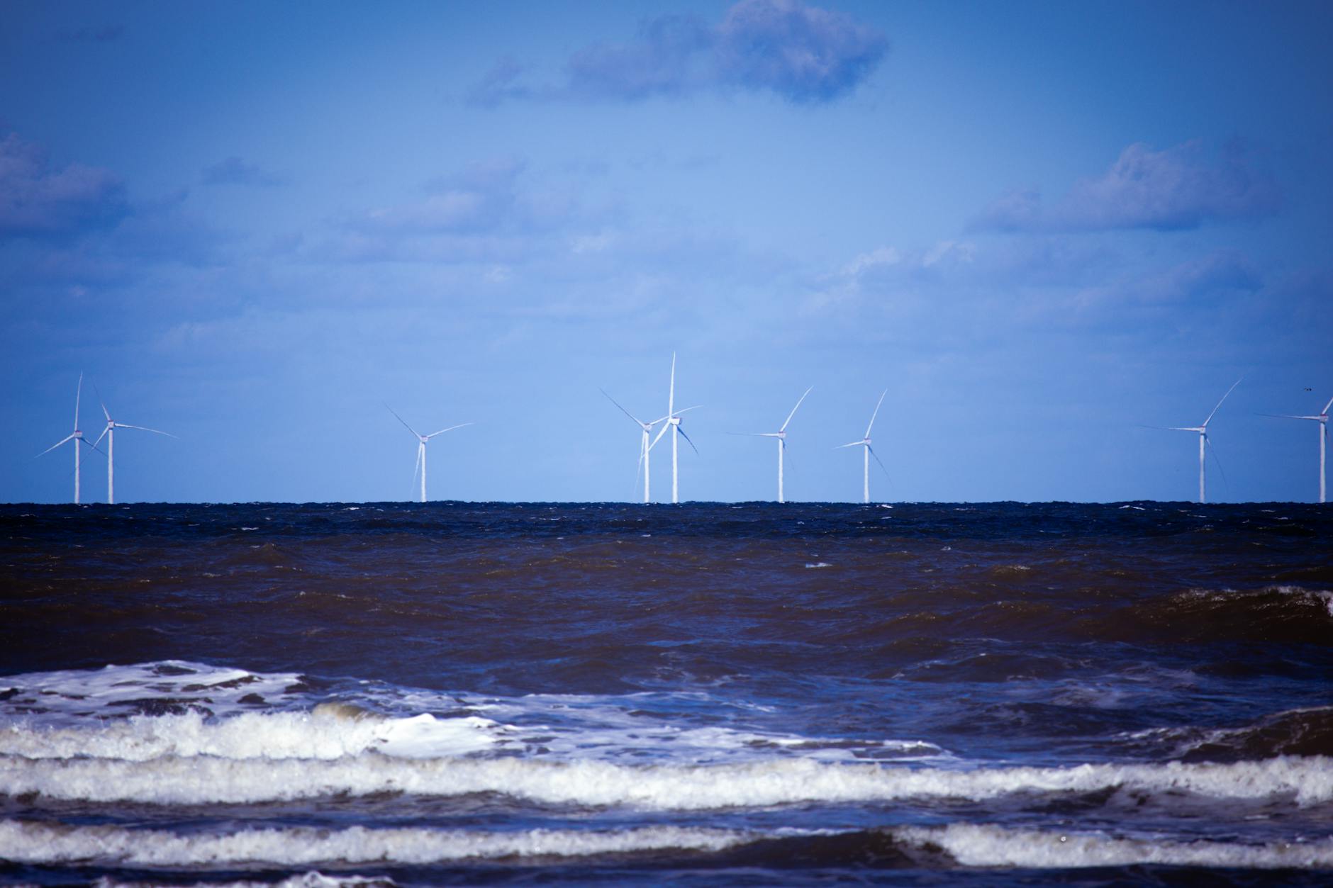 Offshore wind turbines generating sustainable energy over a calm ocean under a clear blue sky.