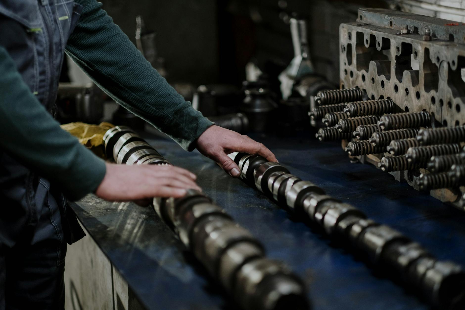 Worker handling camshafts and cylinder head in a mechanic workshop.