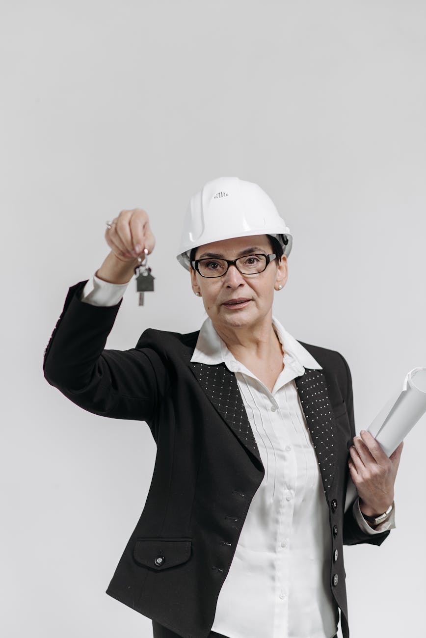Professional female real estate agent in a suit holding keys and documents against a white background.