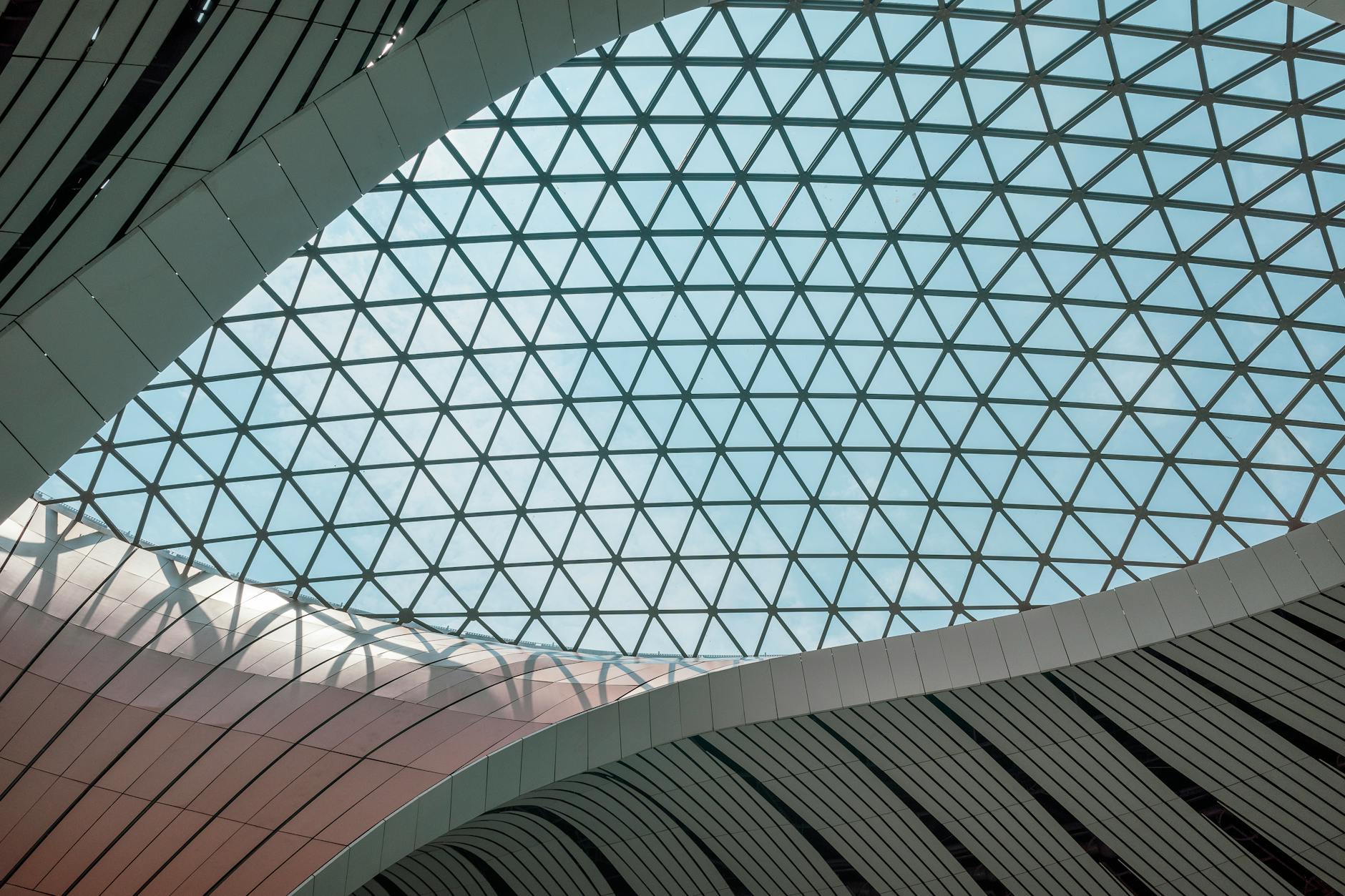 Modern architectural design showcasing a large geometric glass roof with steel structures indoors.