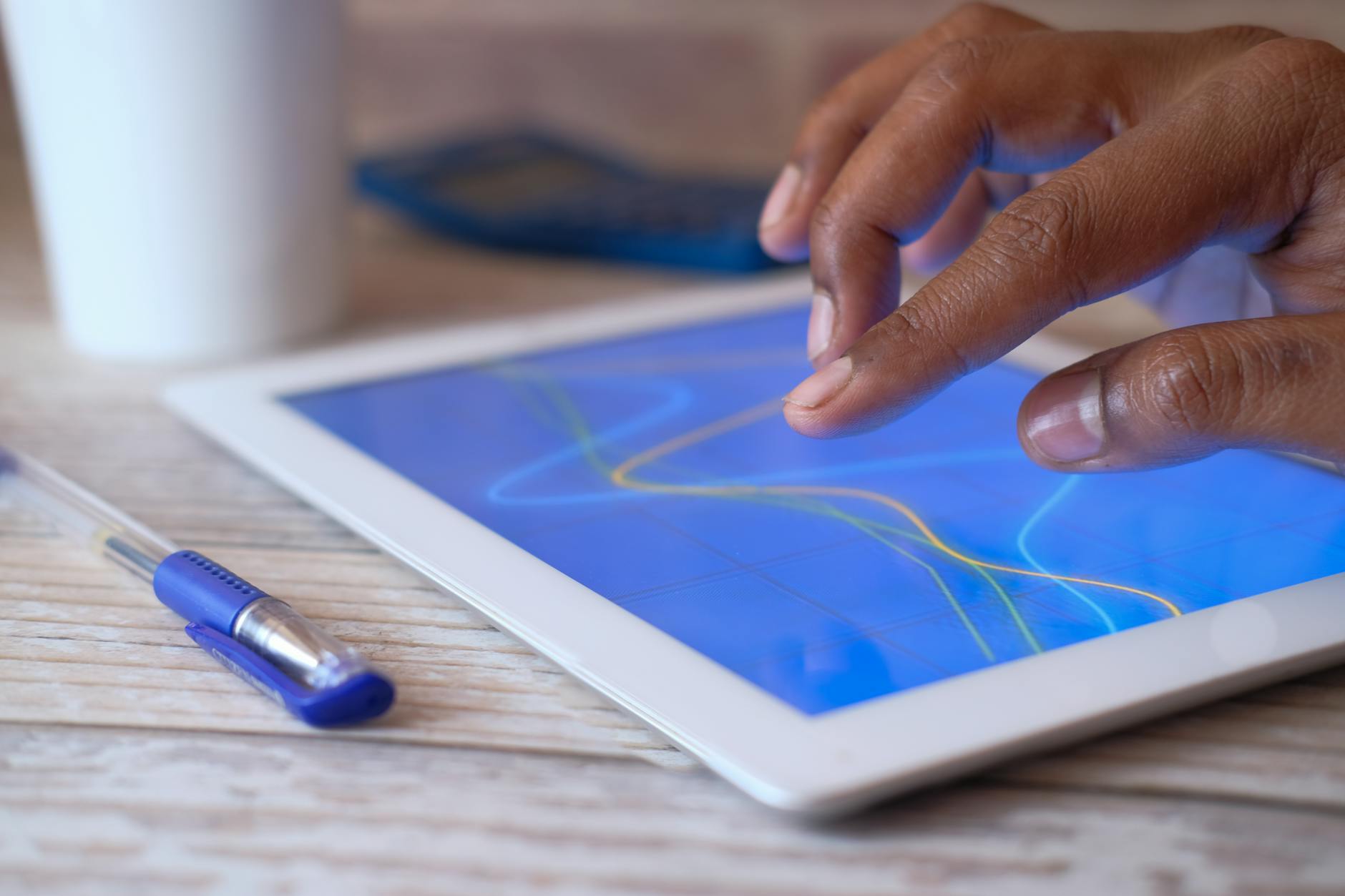 A hand interacting with a digital tablet on a wooden table, showcasing modern technology.