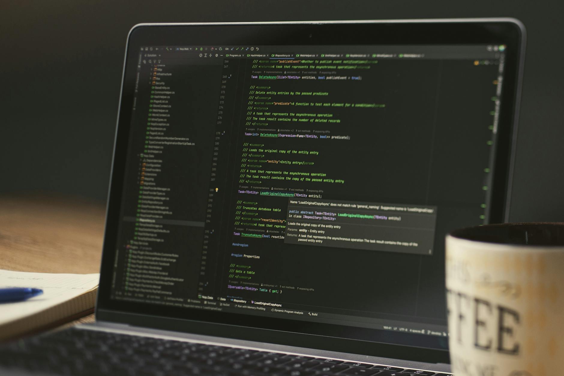 A close-up of a laptop displaying code in a dimly lit room with a coffee mug nearby.