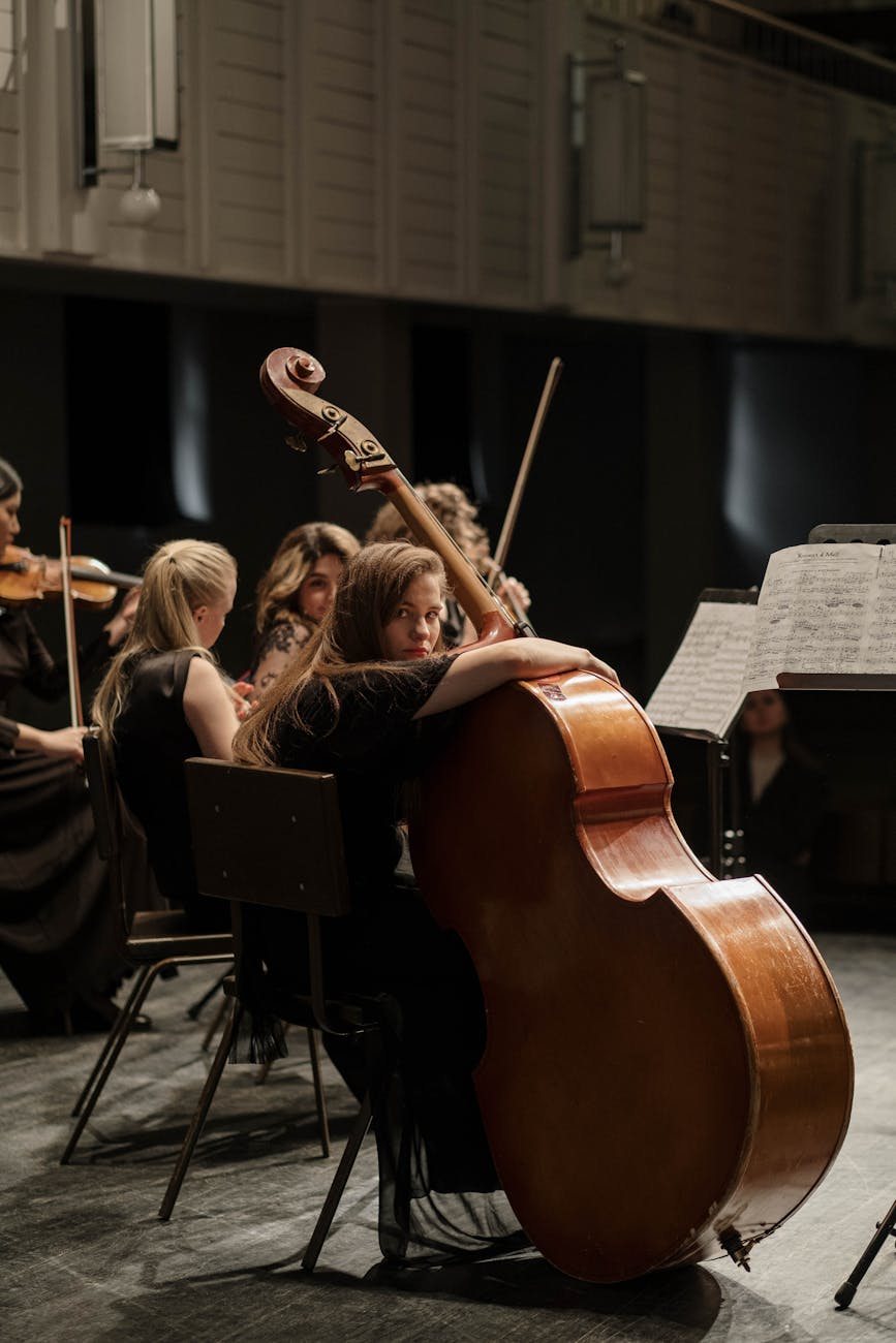 Woman playing cello in an orchestral performance in a concert hall setting.