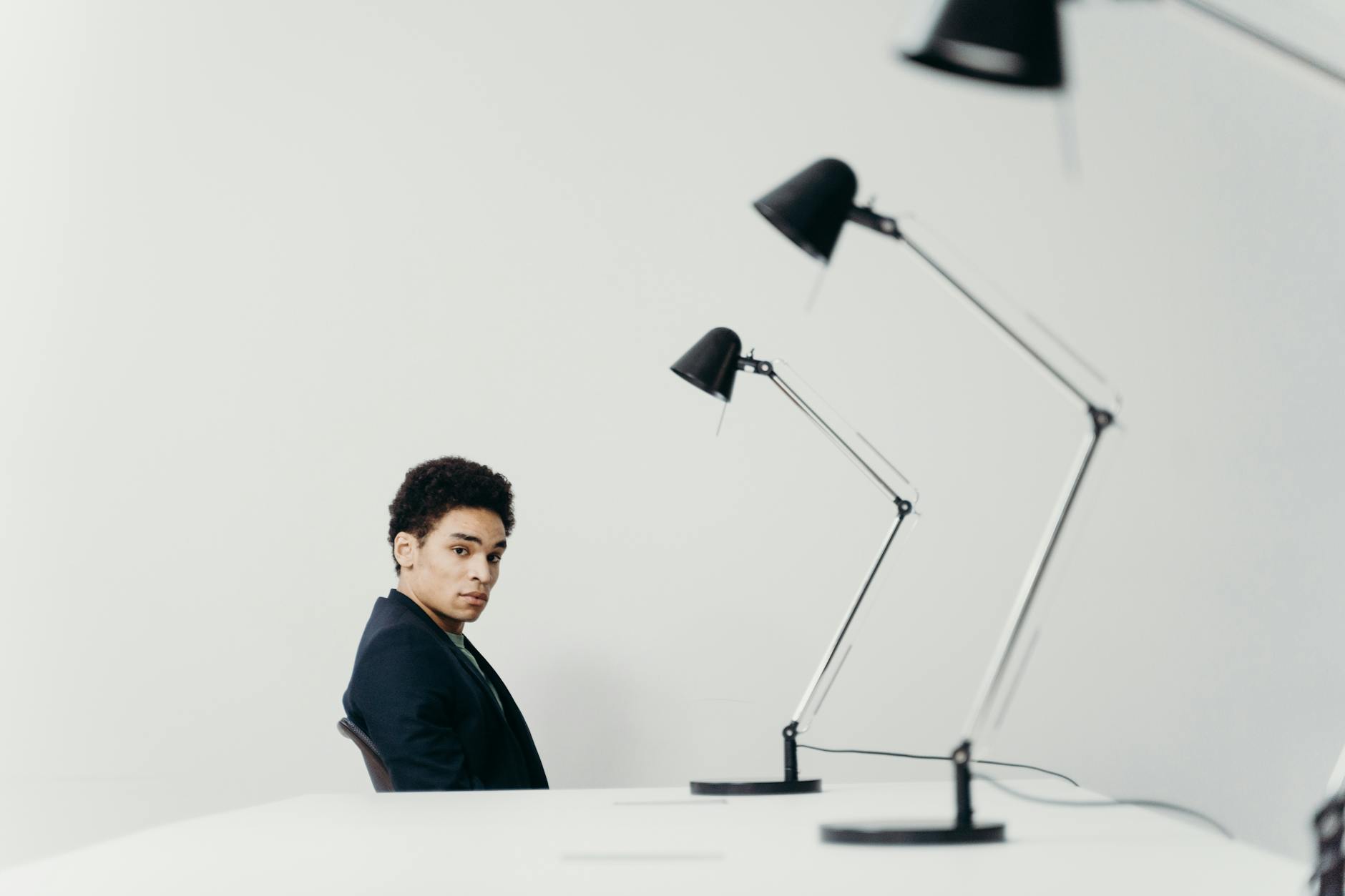 Young man in modern office setting with sleek lamps and minimal design.