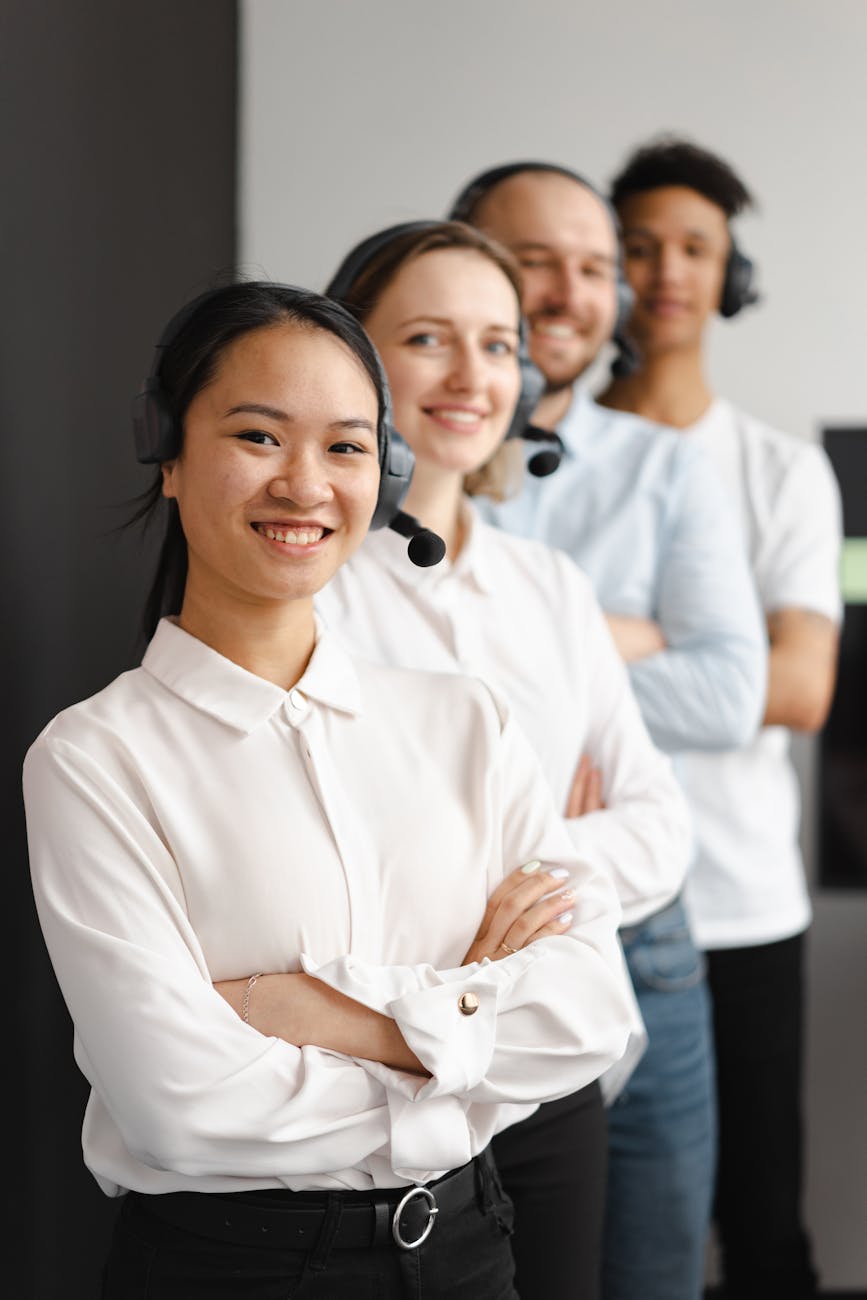 Smiling diverse customer service team with headsets standing in a line indoors.