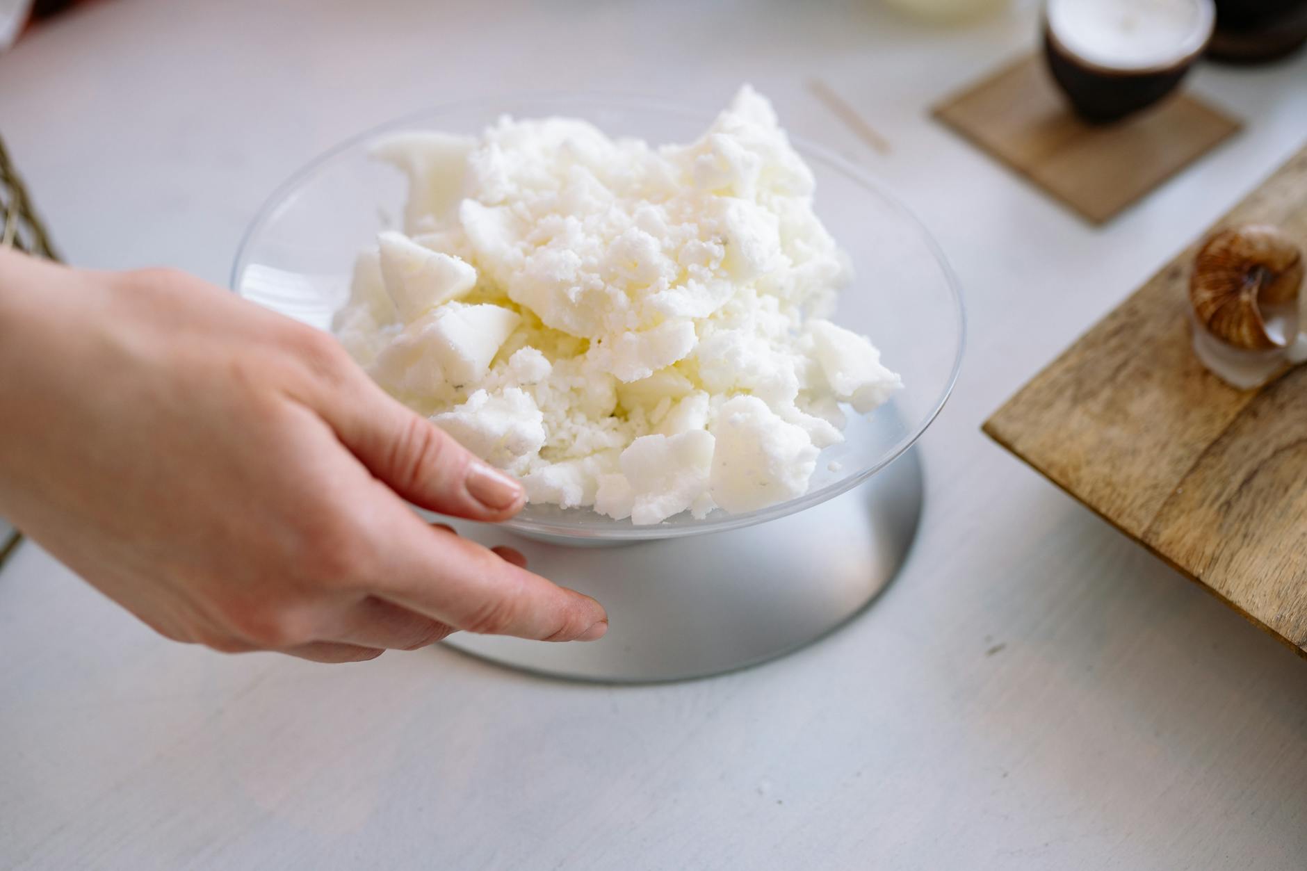 Close-up of a hand weighing candle wax indoors for crafting.
