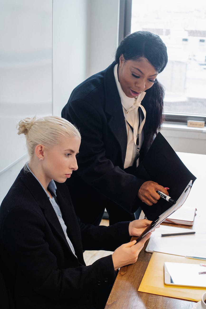 Two businesswomen discussing a document in a bright office space, showcasing teamwork and collaboration.