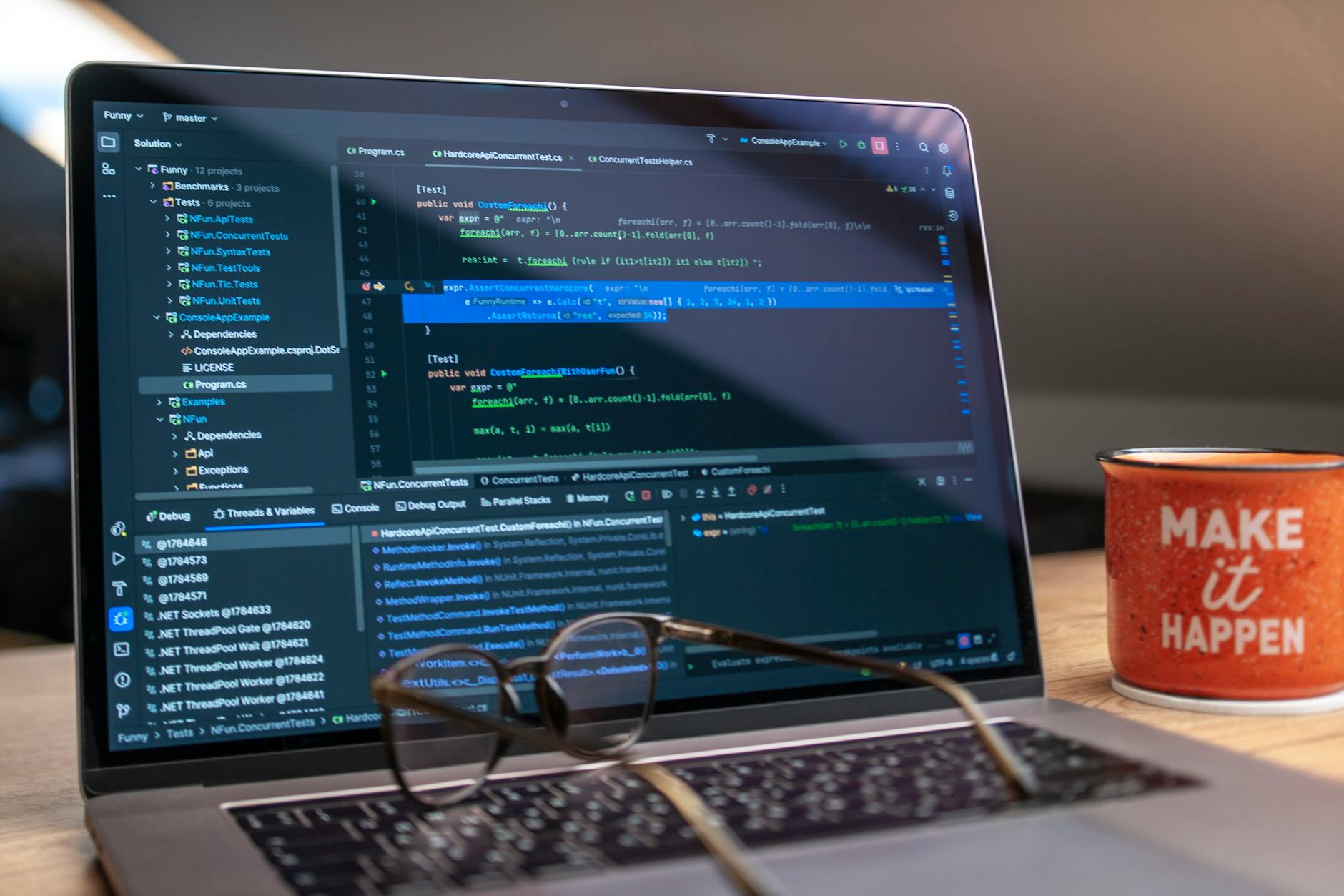 A laptop displaying code editor with a motivational mug that reads 'Make It Happen' on a workspace.