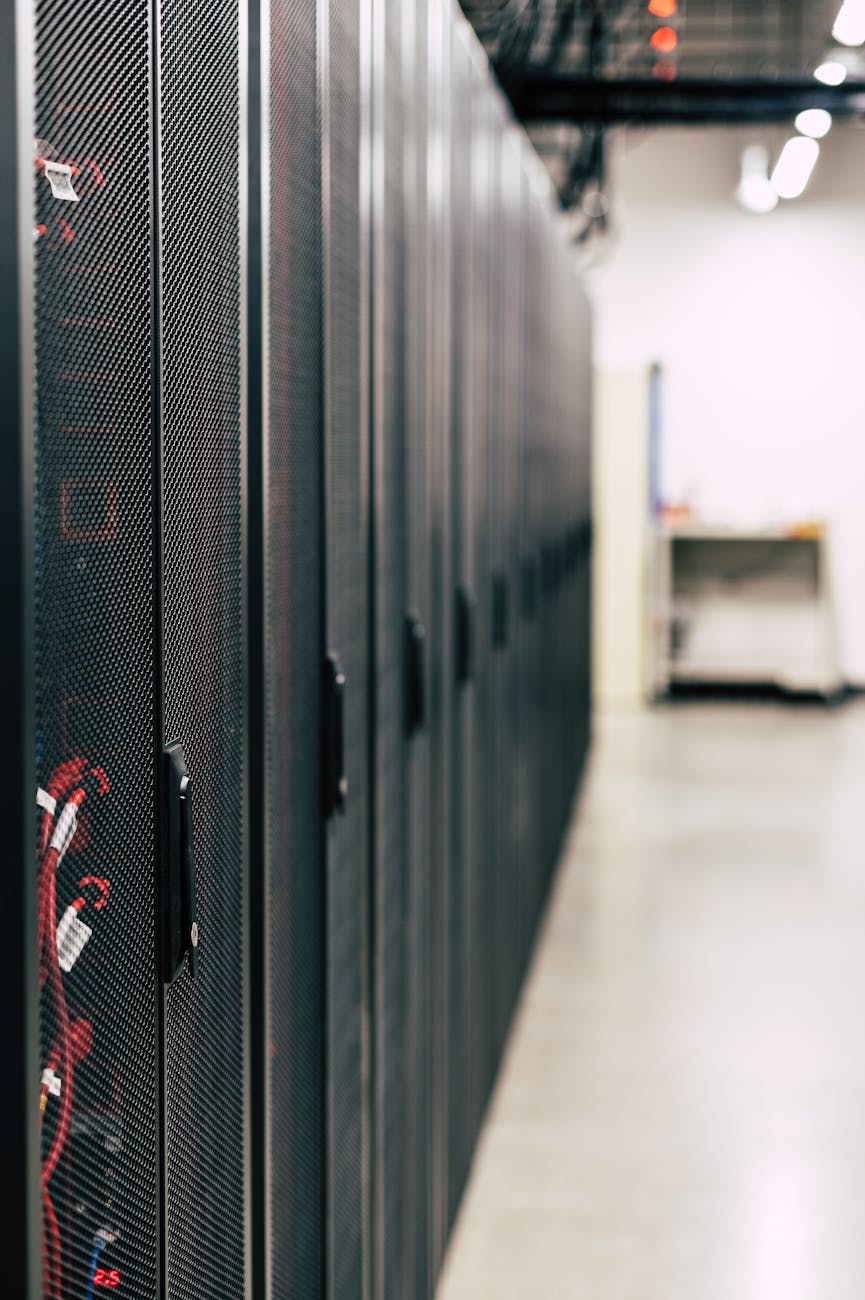 Metal black cabinets with servers inside with red wires connected standing in row in lighted room