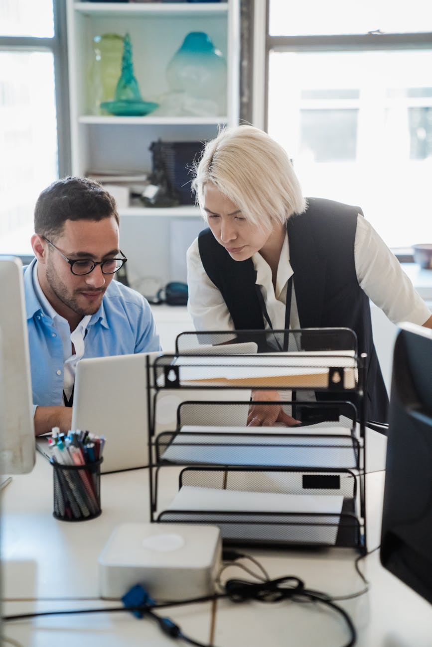 Two colleagues collaborate at a laptop in a bright, modern office environment, fostering teamwork and productivity.