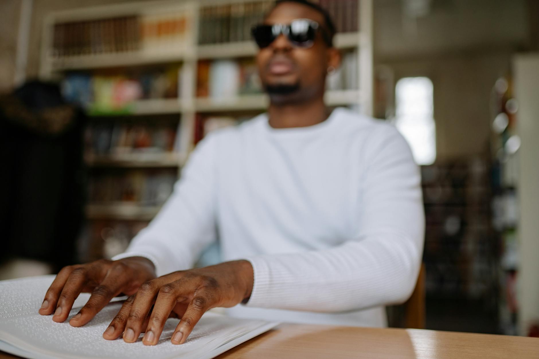 A blind man in a library reading a book using the Braille system, focused on education.