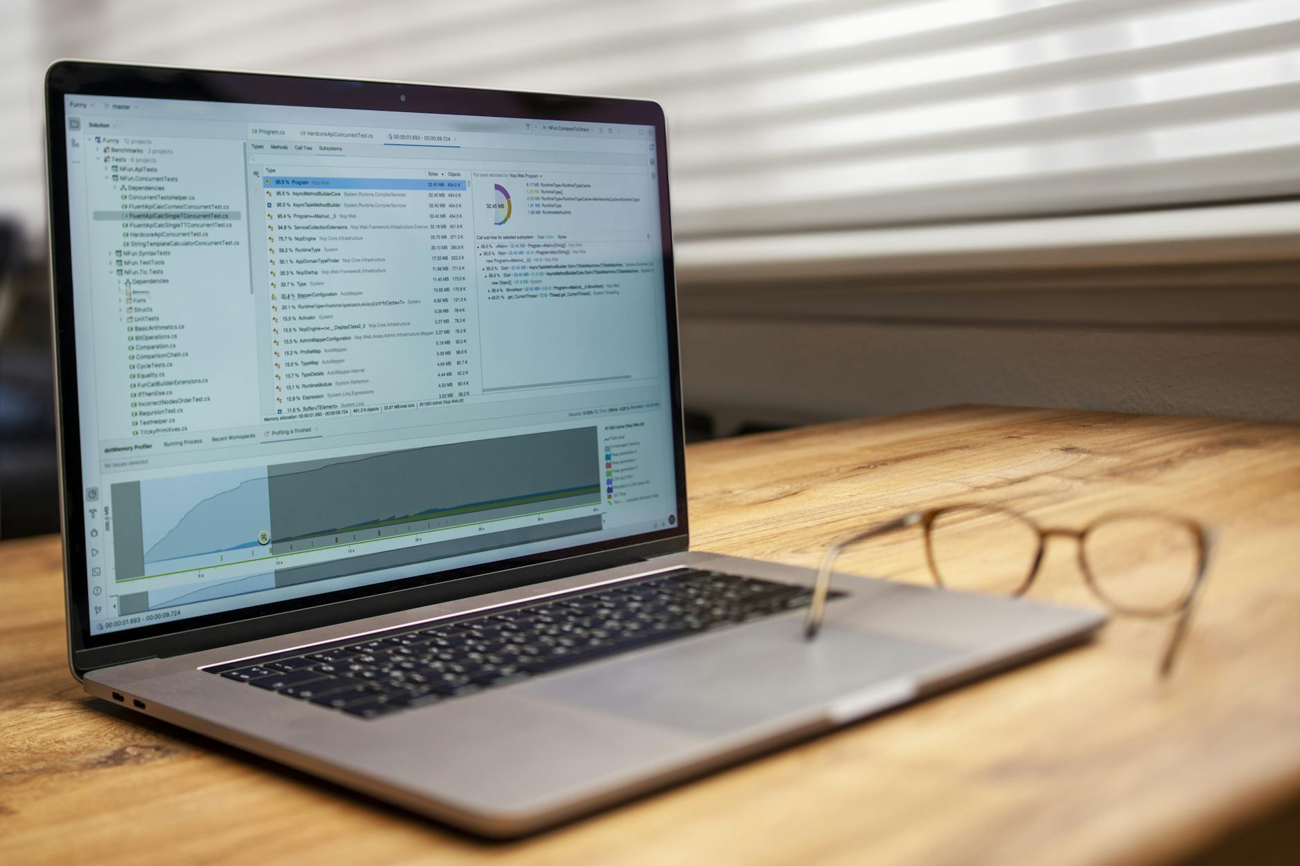 Modern laptop on a wooden desk displaying analytical software with eyeglasses nearby, indoor shot.