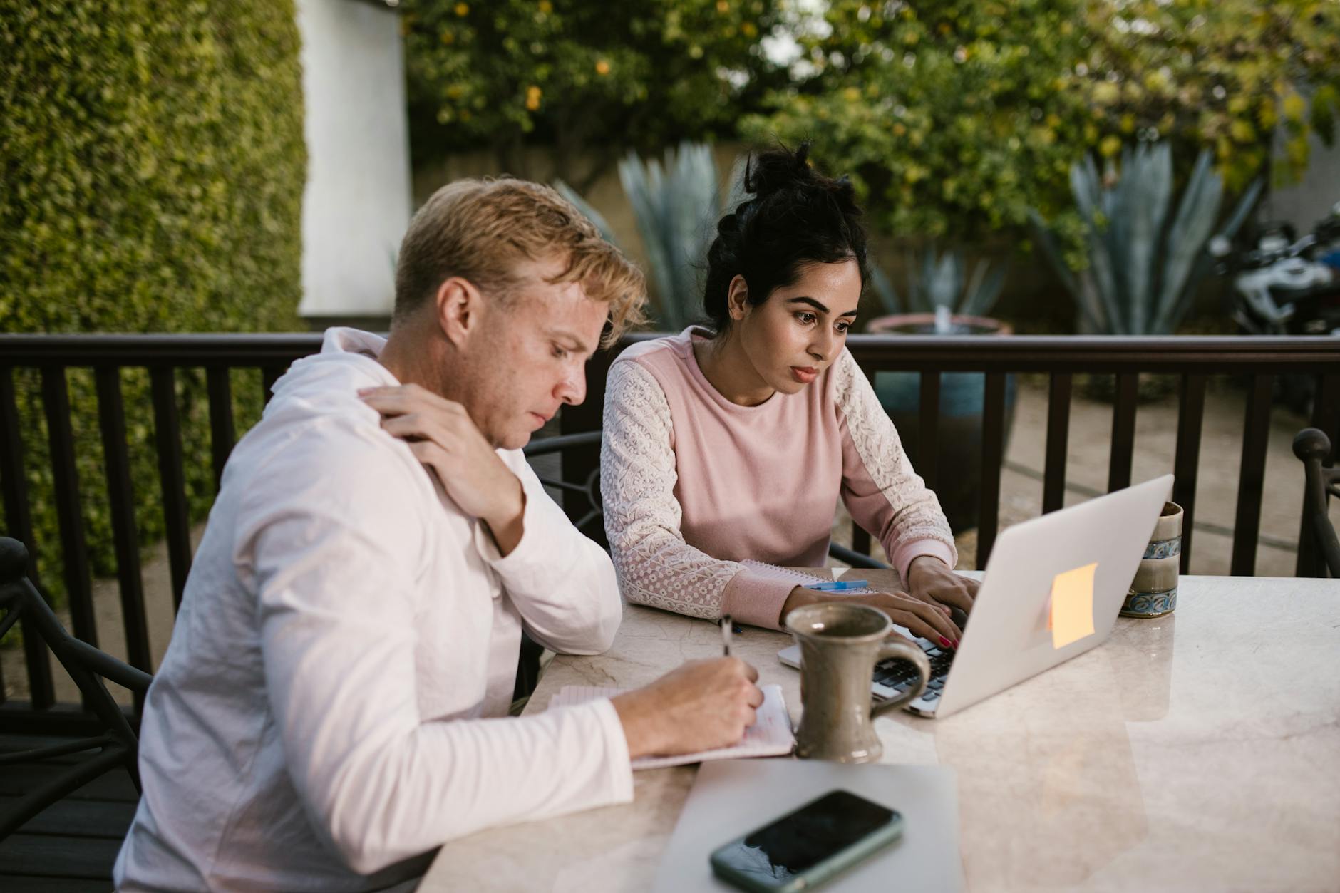 Two adults working together on a laptop outdoors, focusing on a project.